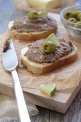 Breakfast: bread with chicken liver pate served with a slice of lime and green olive on wooden background.