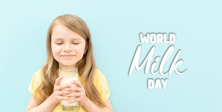 World milk day. Cute little girl with her eyes closed drinks white milk from transparent glass on blue background. Baby child with cup of milk. Banner