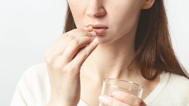 Close up cropped image of young caucasian girl holding pill and glass of fresh water, taking medicine for headache, abdominal pain or taking vitamins, sedatives, health care concept