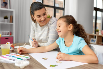 Fototapeta premium family, motherhood and leisure concept - happy smiling mother spending time with her little daughter drawing or painting wooden chipboard items with colors at home