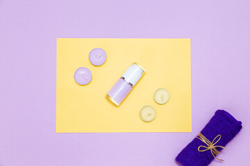 Scented candles, towel and lotion on a yellow and purple background.