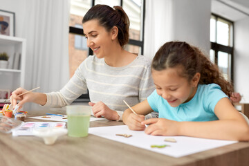 family, motherhood and leisure concept - happy smiling mother spending time with her little daughter drawing or painting wooden chipboard items with colors at home