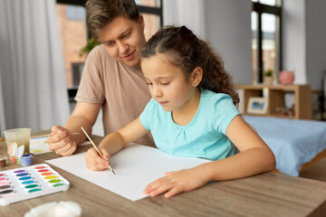 family, motherhood and leisure concept - happy smiling father spending time with his little daughter and drawing with colors at home