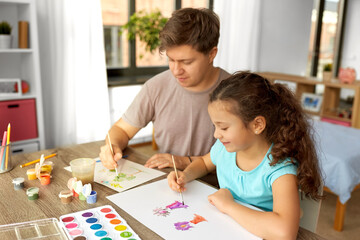 Obraz premium family, motherhood and leisure concept - happy smiling father spending time with his little daughter and drawing with colors at home