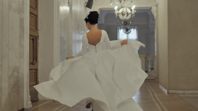 A girl in a fluffy dress runs down the hall. The bride runs down the hall holding her dress. Running bride in a lush white dress.