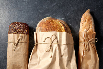 food, baking and cooking concept - close up of bread in paper bags on table over dark background