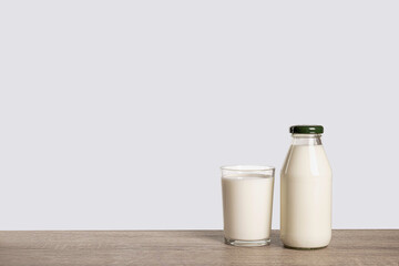 Bottle and glass of milk on wooden table with grey background.