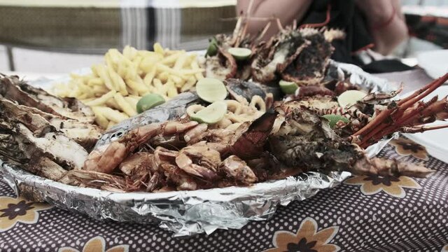 Plate with seafood. Large platter of deliciously cooked squid, shrimp, crab, lobster, octopus and tuna is served on a table near beach. An exotic lunch for tourists in Africa. African style. Zanzibar