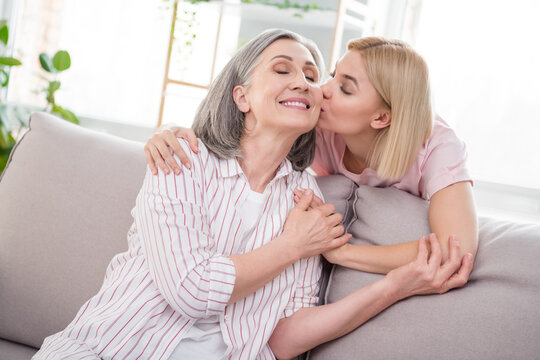 Photo of happy mother and daughter good mood sit sofa kiss cheek trust care indoors inside house home flat