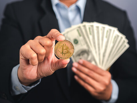 Investor guy showing a bitcoin golden coin and US banknote while standing in the studio. Close-up photo. Space for text. Virtual cryptocurrency and future money concept