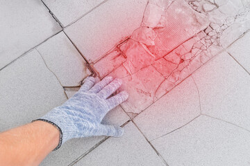 Hand of male construction worker in protective gloves examines old broken tile floor background. Renovation concept