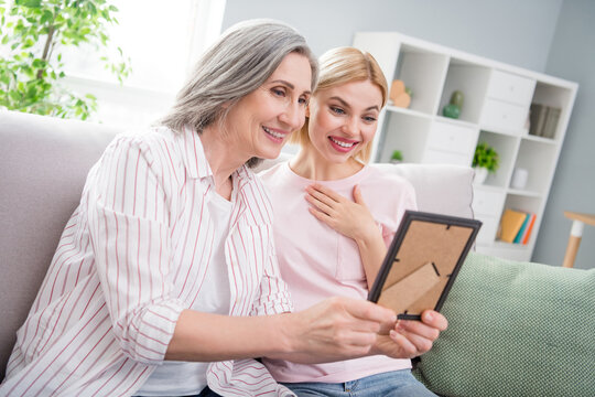 Photo of happy positive amazed excited family mom and daughter sit sofa look frame picture indoors inside house