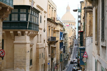 Fototapeta na wymiar Valletta, Malta, March 17, 2021: St. Paul's Anglican Cathedral as seen from the top of the narrow Old Mint Street in Valletta with hanging balconies on either side.