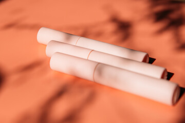 pink closed tubes of mascara, eyeliner, lip gloss, liquid lipstick on a peach background with shadows, copy space