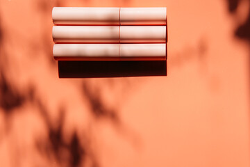 pink closed tubes of mascara, eyeliner, lip gloss, liquid lipstick on a peach background with shadows, copy space