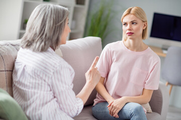 Portrait of two persons sit on sofa look attentively each other pointing finger explain tell teach...