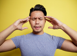 man wearing casual t-shirt dizzy expression holding head isolated on a yellow color background