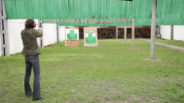 A young man in protective headphones strips from a gun on green targets in the dash. Sports shooting, dangerous firearms, hobbies. outdoors activity general form
