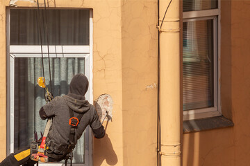 Industrial climber with a hammer removes old cracked plaster