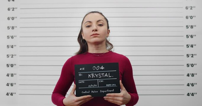 Portrait of female criminal with ponytail holding sign for photo in police department. Crop view of millennial woman posing, raising head and looking to camera.Concept of mugshot.
