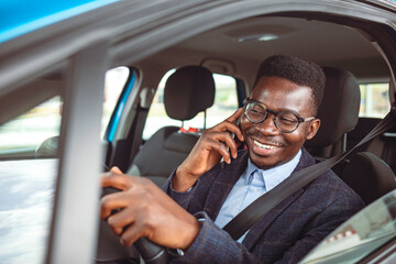 Businessman using mobile phone while driving a car. Nice business talk. Handsome young businessman talking on his smart phone and smiling while sitting on the front seat