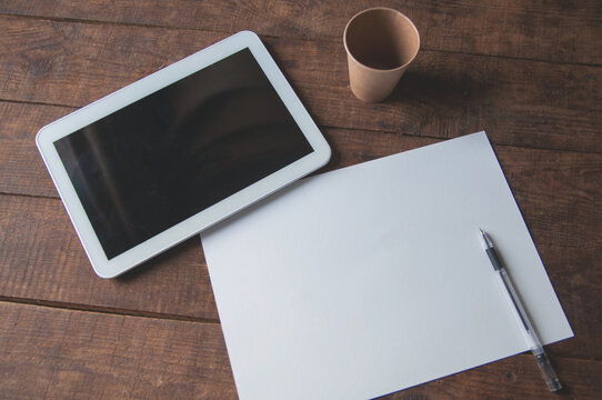 Office workplace with tablet pc on the table. On the table there is a tablet and a white sheet of paper with a pen.