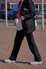 A woman in a black men's suit and white shirt, with fashion accessories, on a sunny spring day.