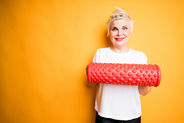 Happy elderly woman standing on yellow background and holding red fascia in her hands smiling at camera