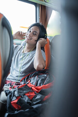 a man wearing headphones smiles while listening to music while sitting by the window in the bus