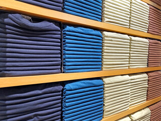Stacks of multicolored cotton T-shirts in a clothing store. Huge stacks of T-shirts lie on wooden shelves.