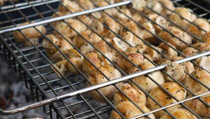 Barbecue of several dozen champignons. They lie on the grill on the fire. The coals are visible from below