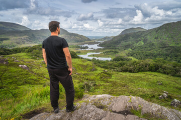 Middle age man standing on a rock and admiring beautiful Ladies View, one of iconic Irish...