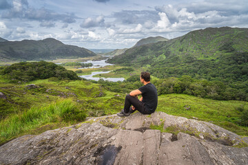 Middle age man sitting on a rock and admiring beautiful Ladies View, one of iconic Irish viewpoints, Lakes of Killarney, Rink of Kerry, Ireland © Dawid