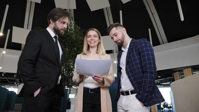 Young creative designers discuss work issues in a futuristic building. Employees hold a marketing plan to develop a business proposal smiling and having a conversation.