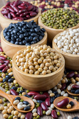 Various grains such as soybeans, black beans, red beans, dried corn in a wooden cup on a wooden table background.