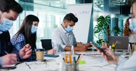 Group of young company apprentices workers receive professional training, sitting around conference table focused on doing task. Business people wearing medical masks during corporate meeting.