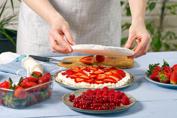 woman baker add a new layer of meringue base in strawberry cake. Homemade strawberries cake made from meringue cake and cream with strawberries. home cooking concept