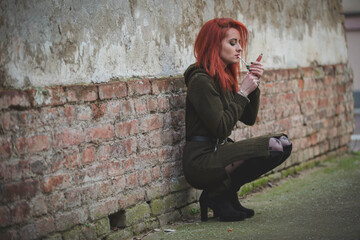 Attractive young Caucasian female in a green dress smoking and posing in front of an old building
