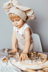 Portrait of a little cook kneading dough in an apron and a chef's hat.