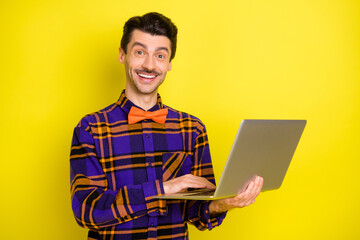 Photo of happy smiling good mood smiling lovely man working in laptop programmer isolated on yellow color background