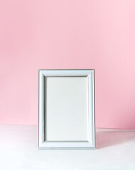 Blank white vertical photo frame mockup. White table and pink wall background. Minimalistic concept with place for text.