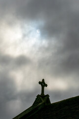 Religious Cross on ancient church building roof in cloud with pale sun