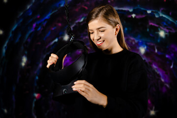 Fototapeta premium The girl puts on virtual reality glasses against the background of space. Young woman wearing virtual reality device. Innovative technologies. Game industry. Mixed media.