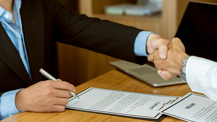 Closed handshake and interview in office focus on employer resume writing tips, good background check of applicants, employers are considering applications in hiring decisions.