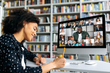 Fototapeta Video call, online education. African American happy female student, learning distantly, watches an online lecture, taking notes, multiracial smiling people on a computer screen, virtual communication obraz
