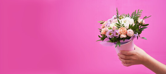 Beautiful bouquet of mixed different flowers in hand on pink background banner with copy space, greeting, gift