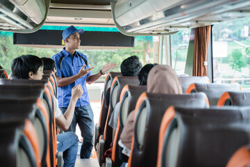 A male bus crew in uniform and a hat briefs passengers with hands-on gesture before leaving for a bus trip