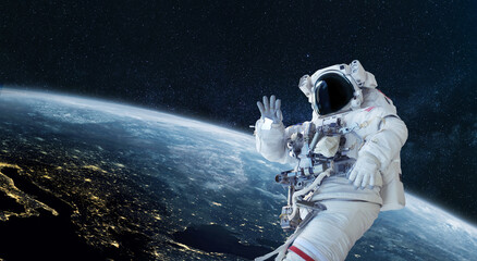 Space man astronaut greets and waves his hand in space on a background of the blue planet Earth....
