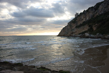 paesaggio marino con montagna sulla destra con torre antica . Tramonto con nuvole suggestive e mare mosso