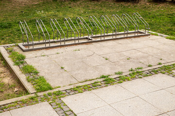 Empty bicycle park with steel shelves and pavement next to green grass.